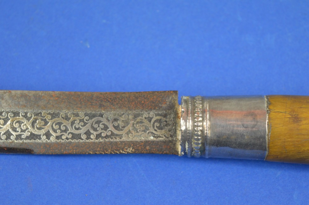 A 19th-century ceremonial knife with a steel blade featuring silver scrollwork inlay, a silver metal collar, and a smooth horn handle. View X