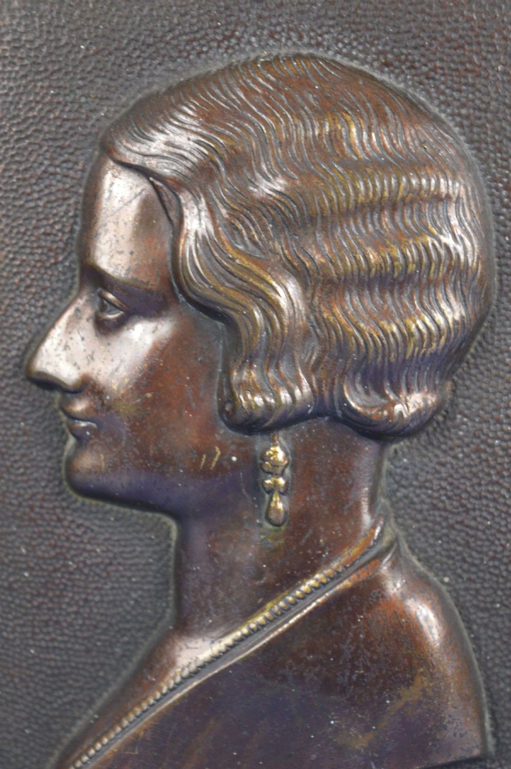An Art Deco dark brown bronze relief plaque featuring a side profile portrait of Queen Astrid against a textured background with inscribed lettering. View III