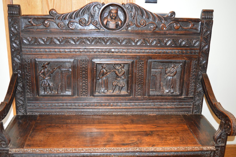 An 18th-century Flemish dark carved oak settle featuring figurative relief panels on the backrest and chest base with scrolled armrests. View II