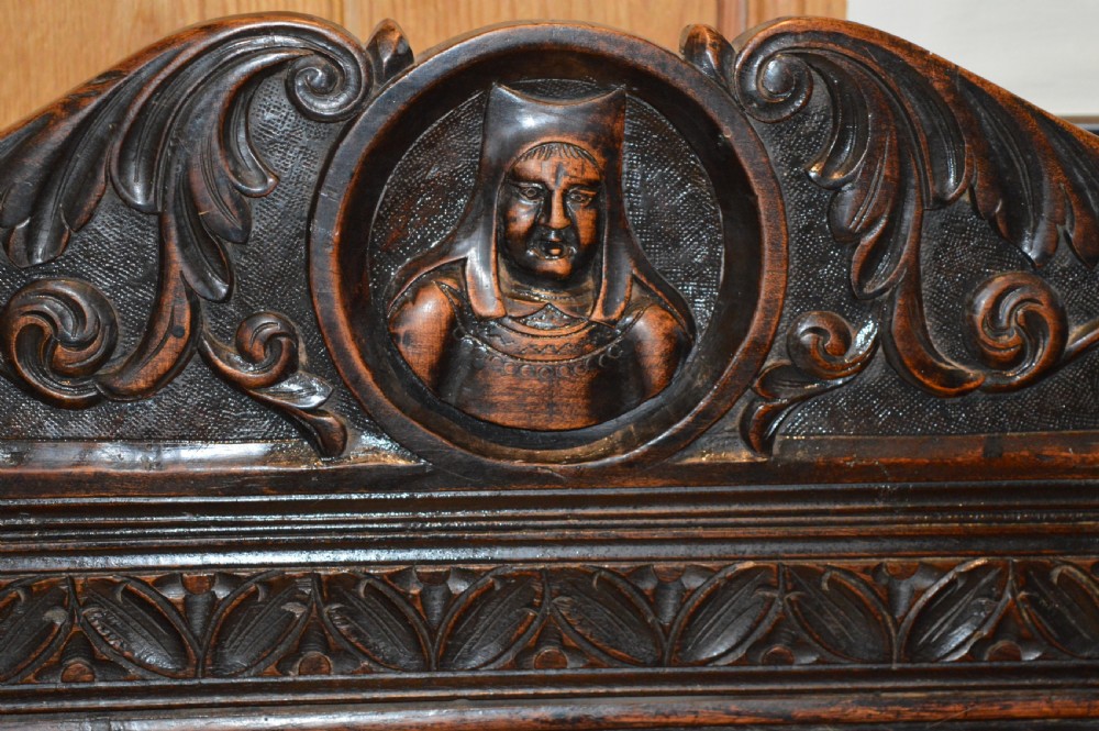An 18th-century Flemish dark carved oak settle featuring figurative relief panels on the backrest and chest base with scrolled armrests. View IV