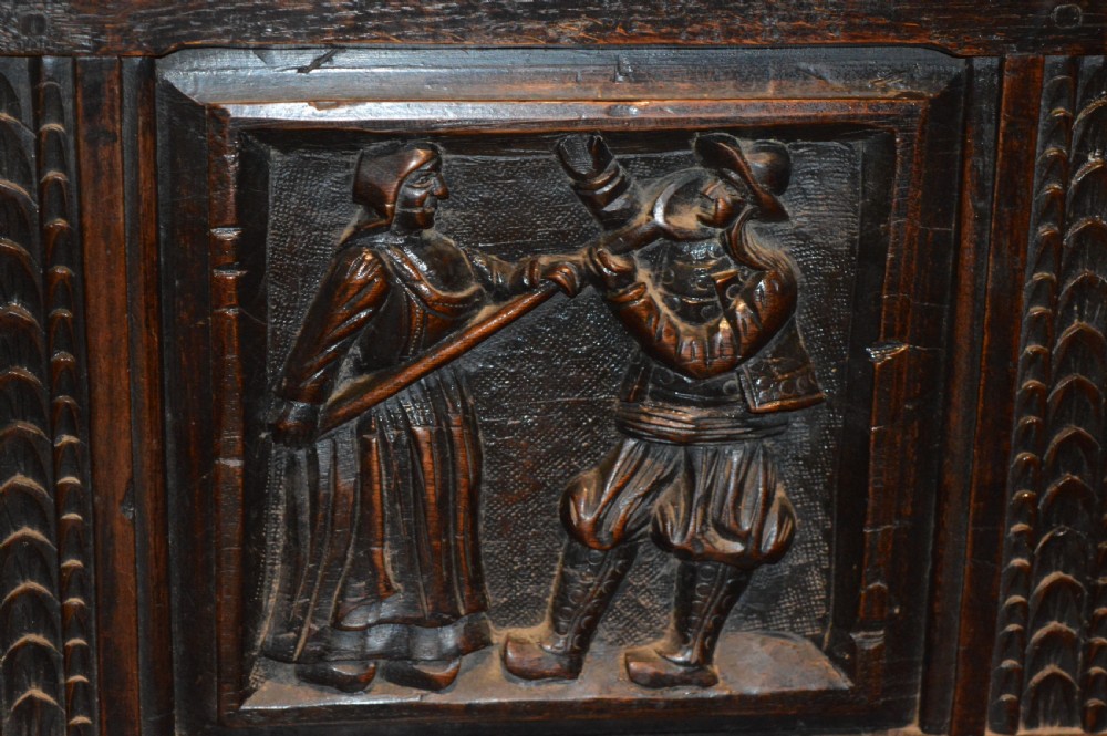 An 18th-century Flemish dark carved oak settle featuring figurative relief panels on the backrest and chest base with scrolled armrests. View V