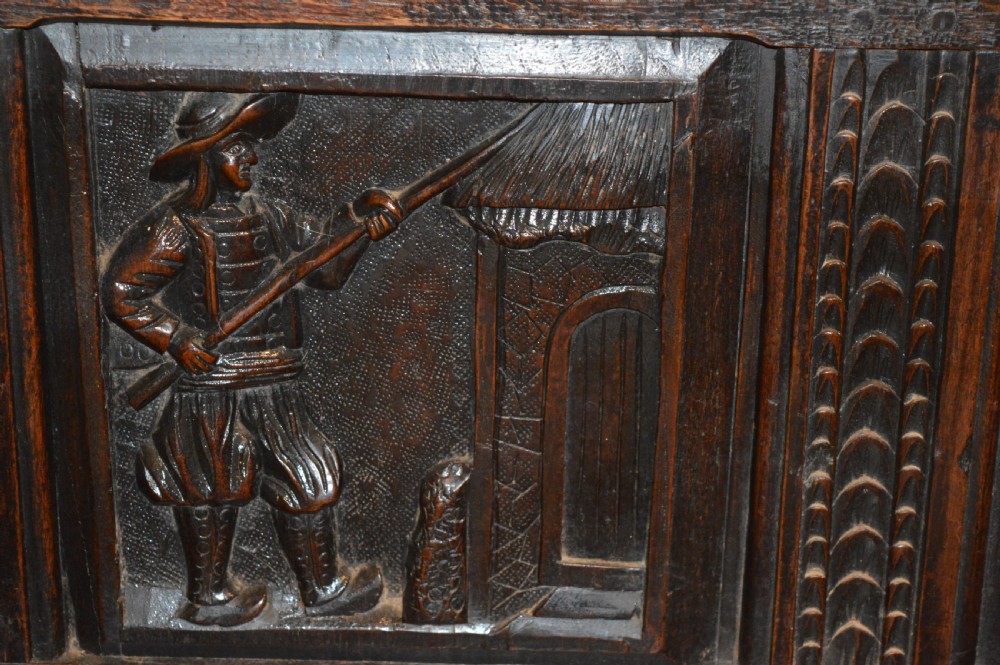 An 18th-century Flemish dark carved oak settle featuring figurative relief panels on the backrest and chest base with scrolled armrests. View VI