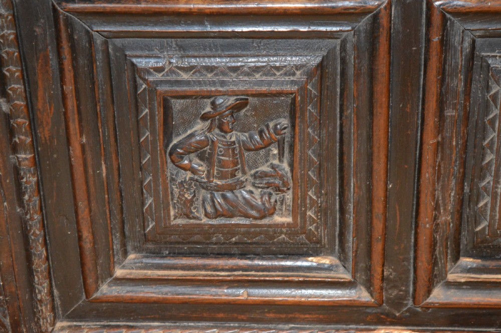 An 18th-century Flemish dark carved oak settle featuring figurative relief panels on the backrest and chest base with scrolled armrests. View IX
