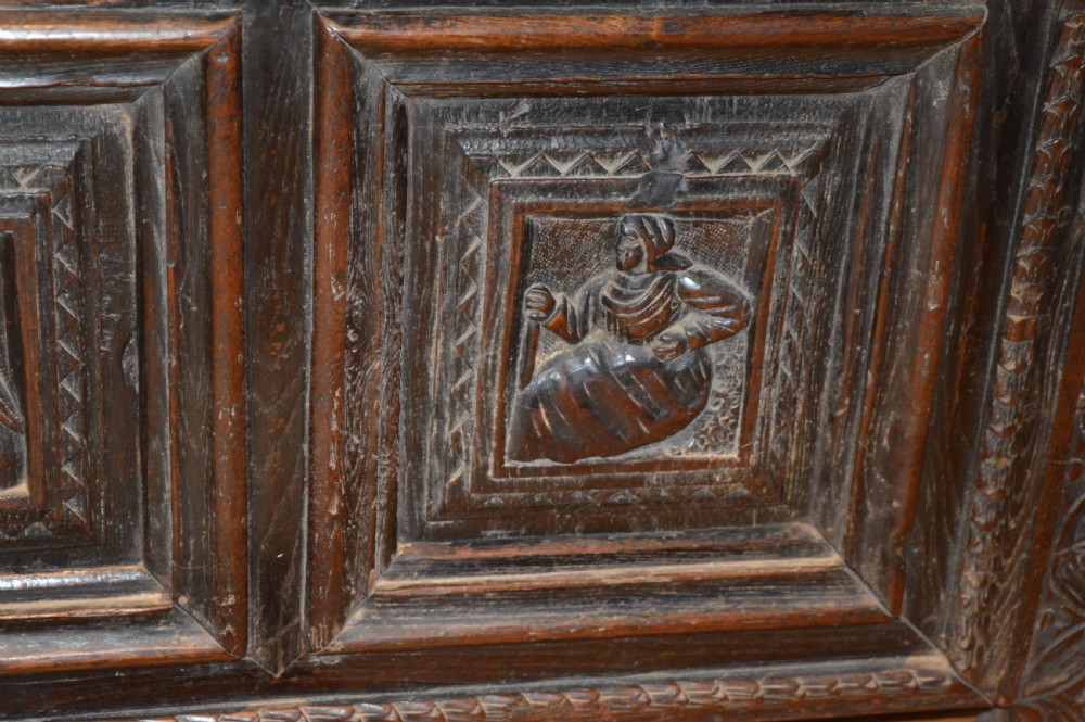An 18th-century Flemish dark carved oak settle featuring figurative relief panels on the backrest and chest base with scrolled armrests. View X