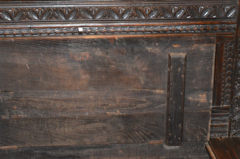 An 18th-century Flemish dark carved oak settle featuring figurative relief panels on the backrest and chest base with scrolled armrests. View XV