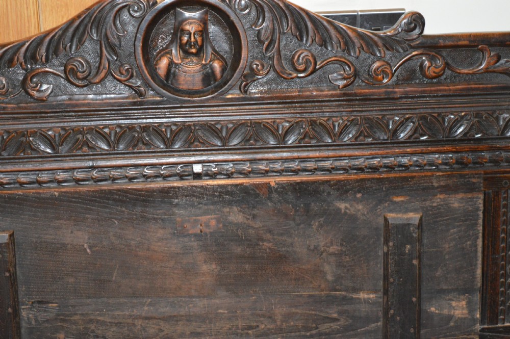 An 18th-century Flemish dark carved oak settle featuring figurative relief panels on the backrest and chest base with scrolled armrests. View XVI
