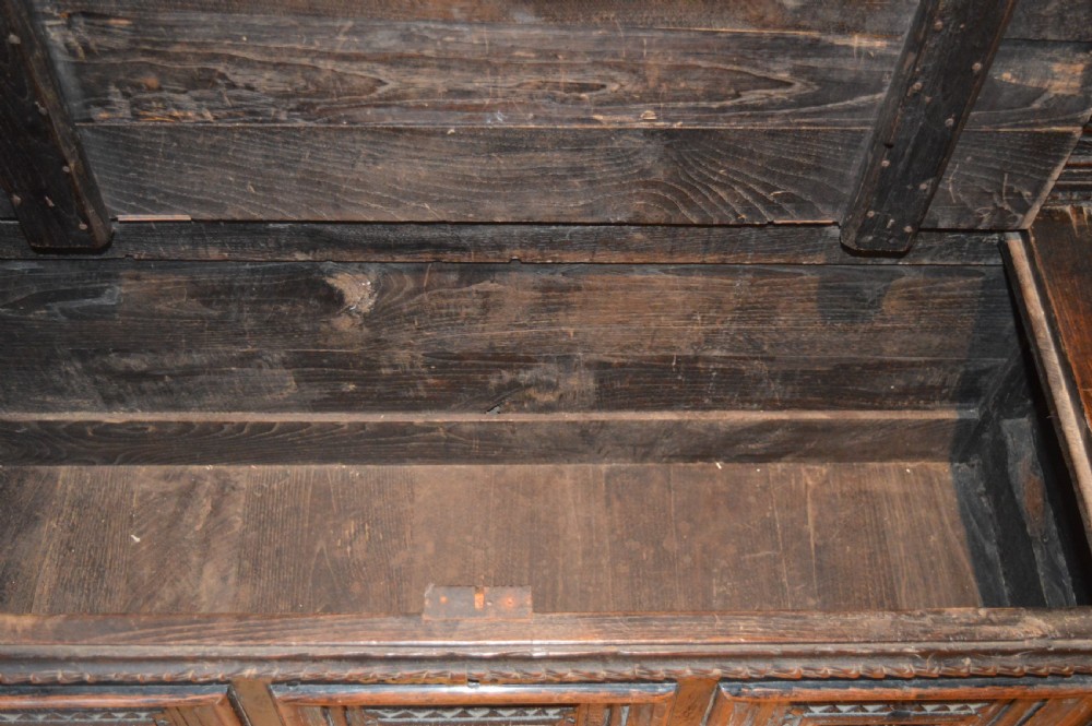 An 18th-century Flemish dark carved oak settle featuring figurative relief panels on the backrest and chest base with scrolled armrests. View XVIII