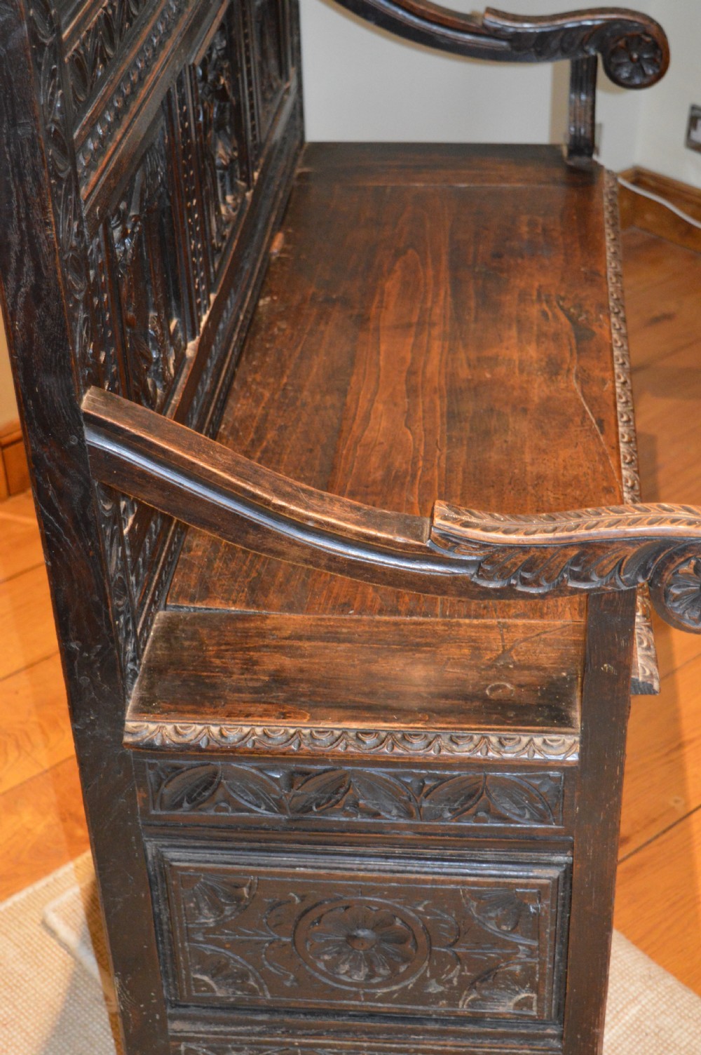 An 18th-century Flemish dark carved oak settle featuring figurative relief panels on the backrest and chest base with scrolled armrests. View XX