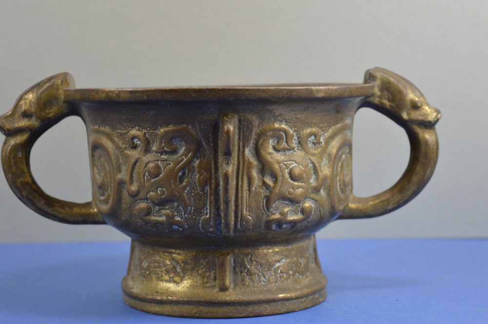 A cast bronze ritual food vessel with two loop handles topped with beast heads, featuring relief carvings and a raised circular base.