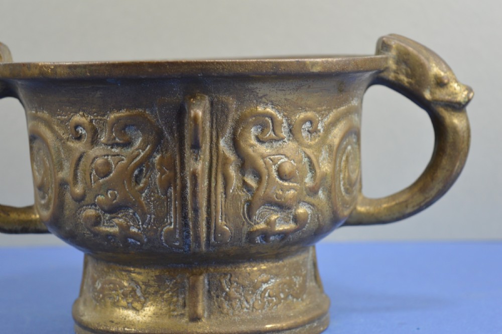 A cast bronze ritual food vessel with two loop handles topped with beast heads, featuring relief carvings and a raised circular base. View II
