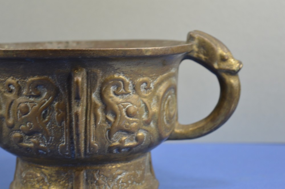 A cast bronze ritual food vessel with two loop handles topped with beast heads, featuring relief carvings and a raised circular base. View III