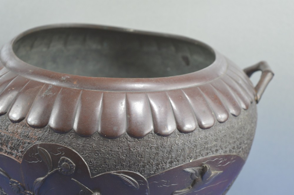 A heavy dark bronze Chinese bowl featuring relief panels with bird and floral motifs, bamboo-style side handles, and a lobed collar over an integral stepped base. View II