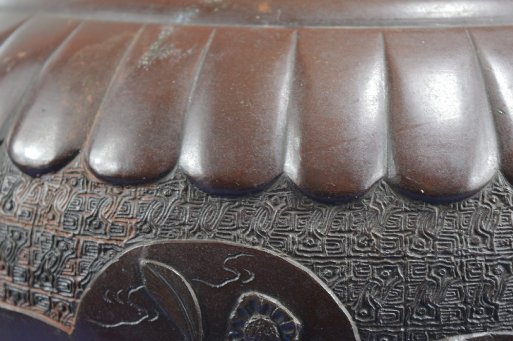 A heavy dark bronze Chinese bowl featuring relief panels with bird and floral motifs, bamboo-style side handles, and a lobed collar over an integral stepped base. View V