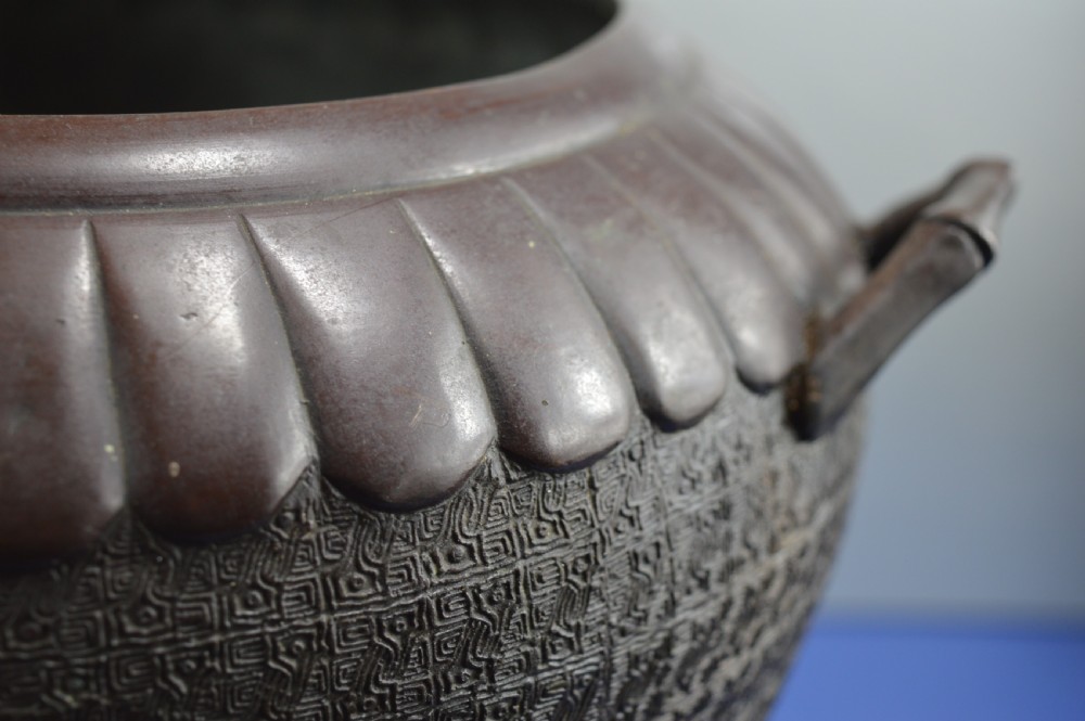 A heavy dark bronze Chinese bowl featuring relief panels with bird and floral motifs, bamboo-style side handles, and a lobed collar over an integral stepped base. View VII
