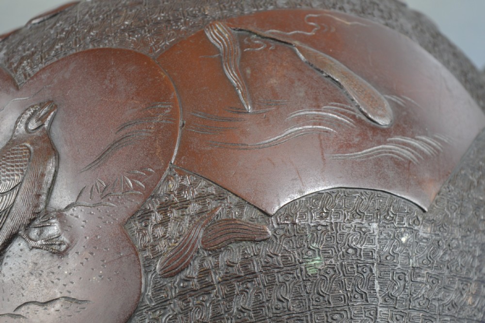 A heavy dark bronze Chinese bowl featuring relief panels with bird and floral motifs, bamboo-style side handles, and a lobed collar over an integral stepped base. View XII