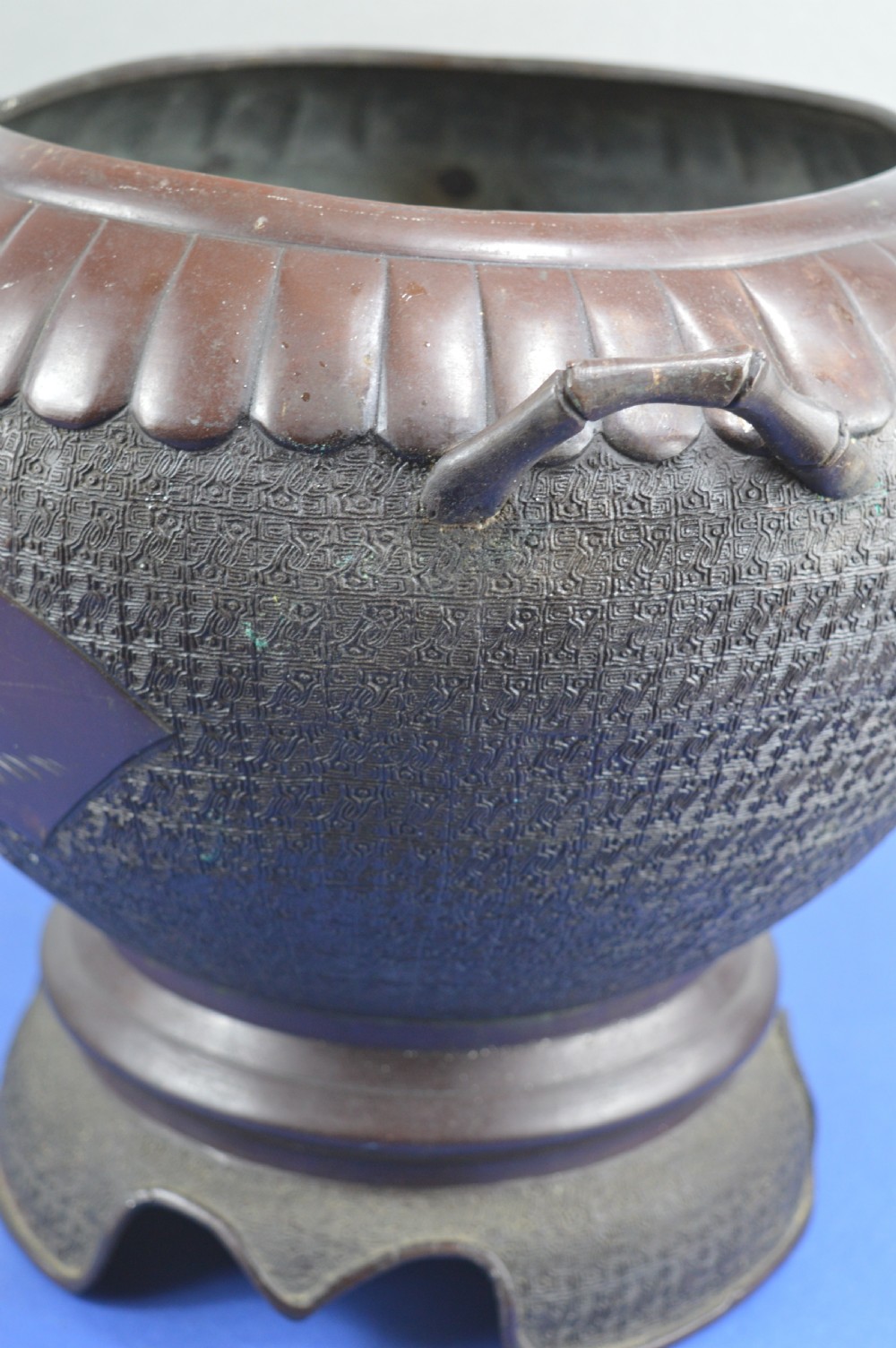 A heavy dark bronze Chinese bowl featuring relief panels with bird and floral motifs, bamboo-style side handles, and a lobed collar over an integral stepped base. View XV