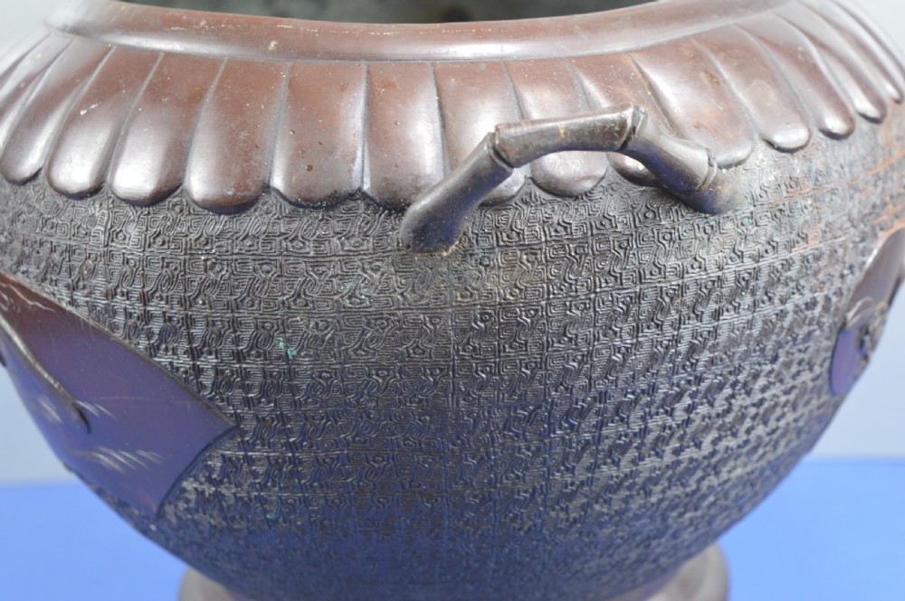 A heavy dark bronze Chinese bowl featuring relief panels with bird and floral motifs, bamboo-style side handles, and a lobed collar over an integral stepped base. View XVI