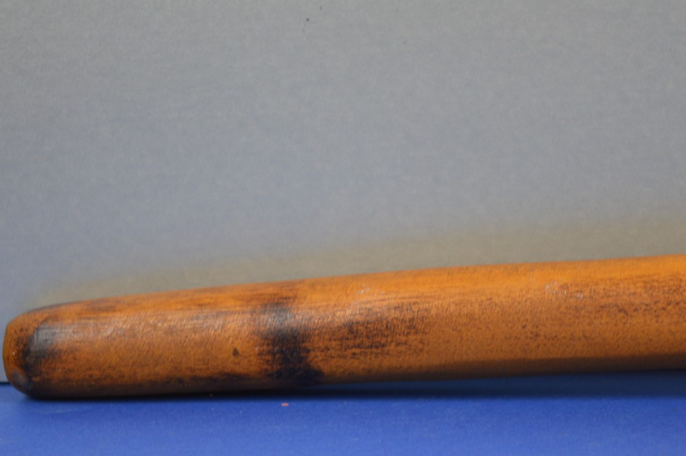 A carved light brown hardwood throwing club featuring a pointed bulbous head with pyrography markings and a smooth tapered shaft. View V