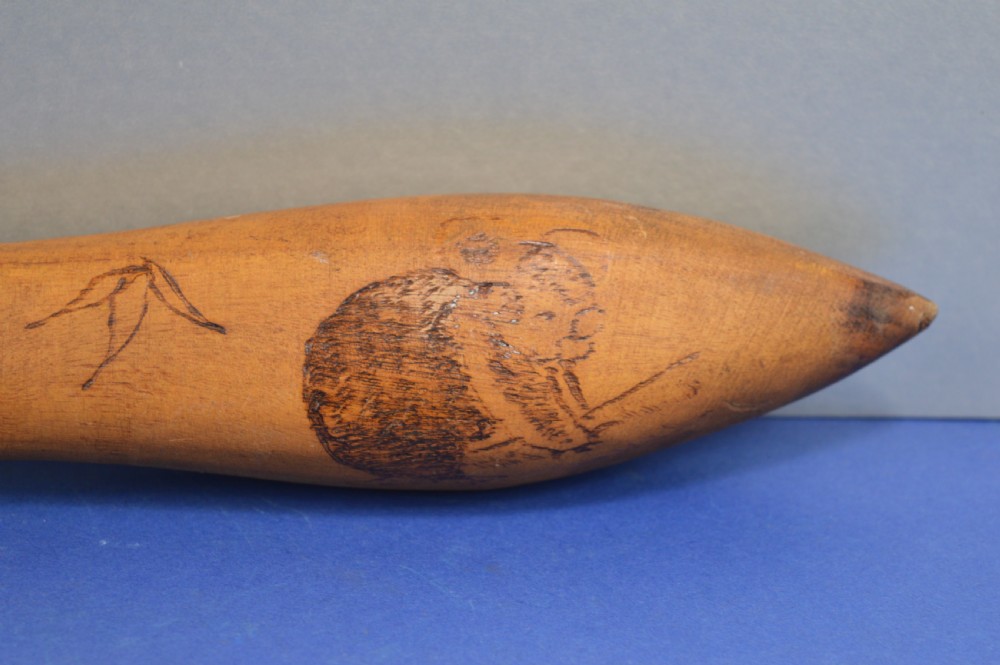 A carved light brown hardwood throwing club featuring a pointed bulbous head with pyrography markings and a smooth tapered shaft. View VI