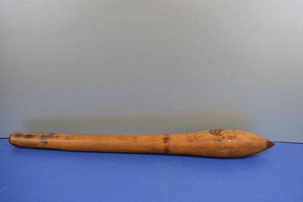 A carved light brown hardwood throwing club featuring a pointed bulbous head with pyrography markings and a smooth tapered shaft. View VII