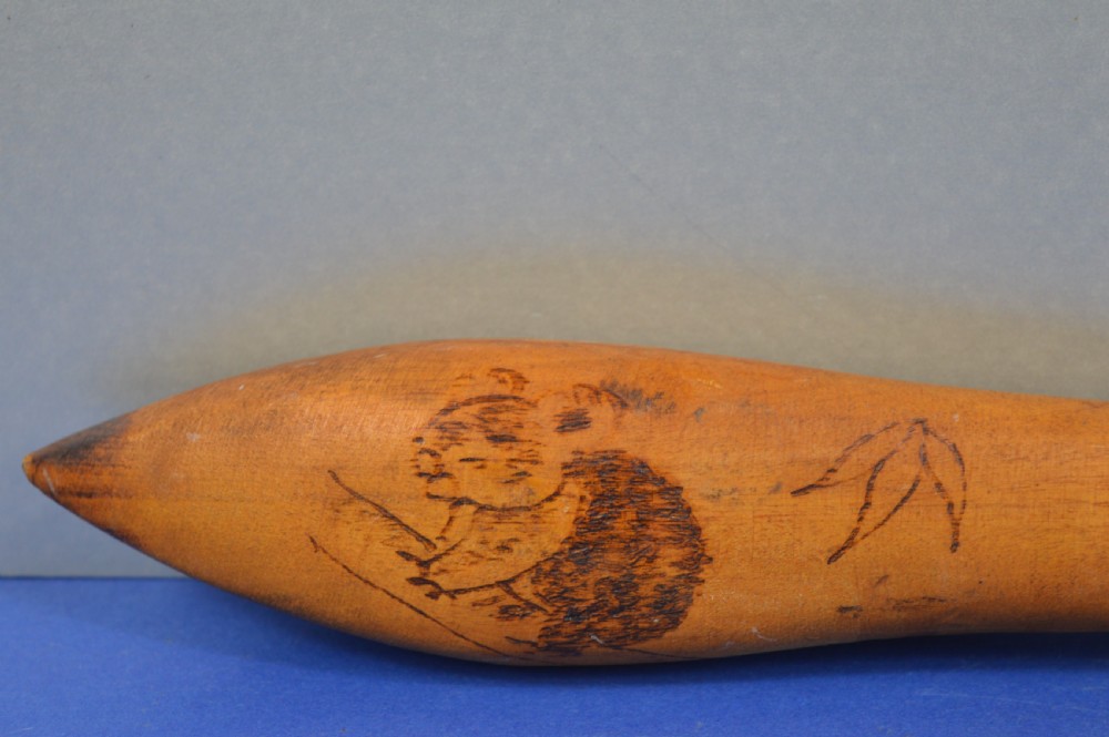 A carved light brown hardwood throwing club featuring a pointed bulbous head with pyrography markings and a smooth tapered shaft. View VIII