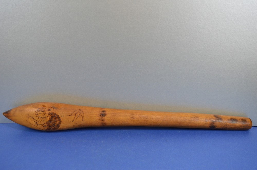 A carved light brown hardwood throwing club featuring a pointed bulbous head with pyrography markings and a smooth tapered shaft. View IX