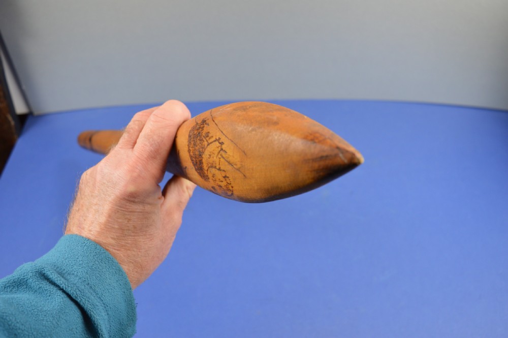 A carved light brown hardwood throwing club featuring a pointed bulbous head with pyrography markings and a smooth tapered shaft. View XI