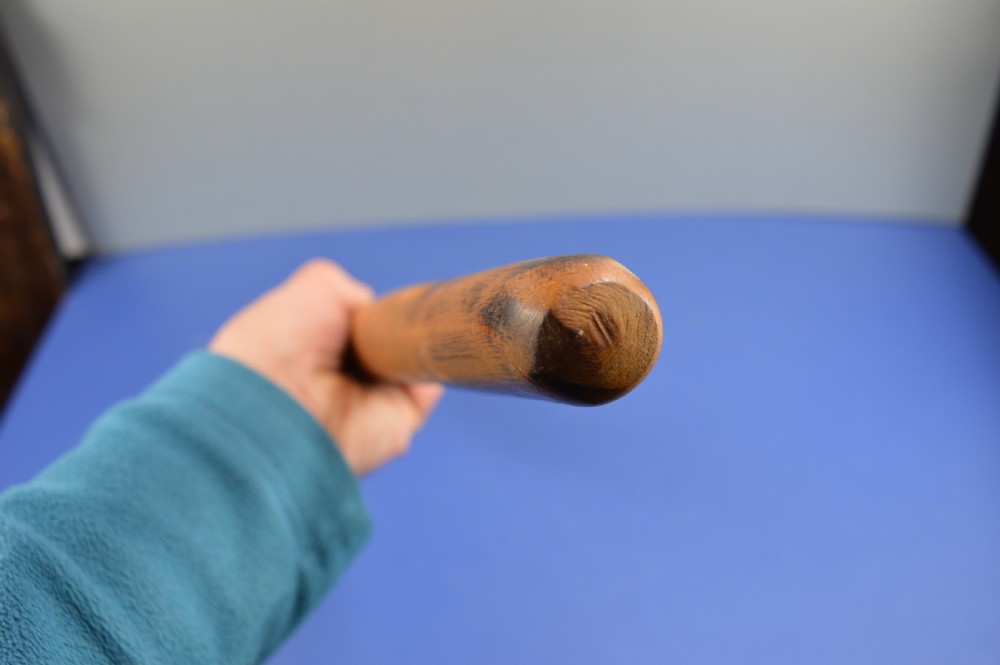 A carved light brown hardwood throwing club featuring a pointed bulbous head with pyrography markings and a smooth tapered shaft. View XII