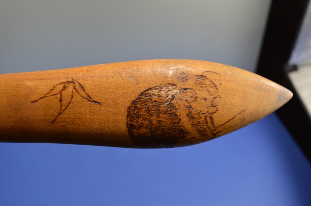 A carved light brown hardwood throwing club featuring a pointed bulbous head with pyrography markings and a smooth tapered shaft. View XIII