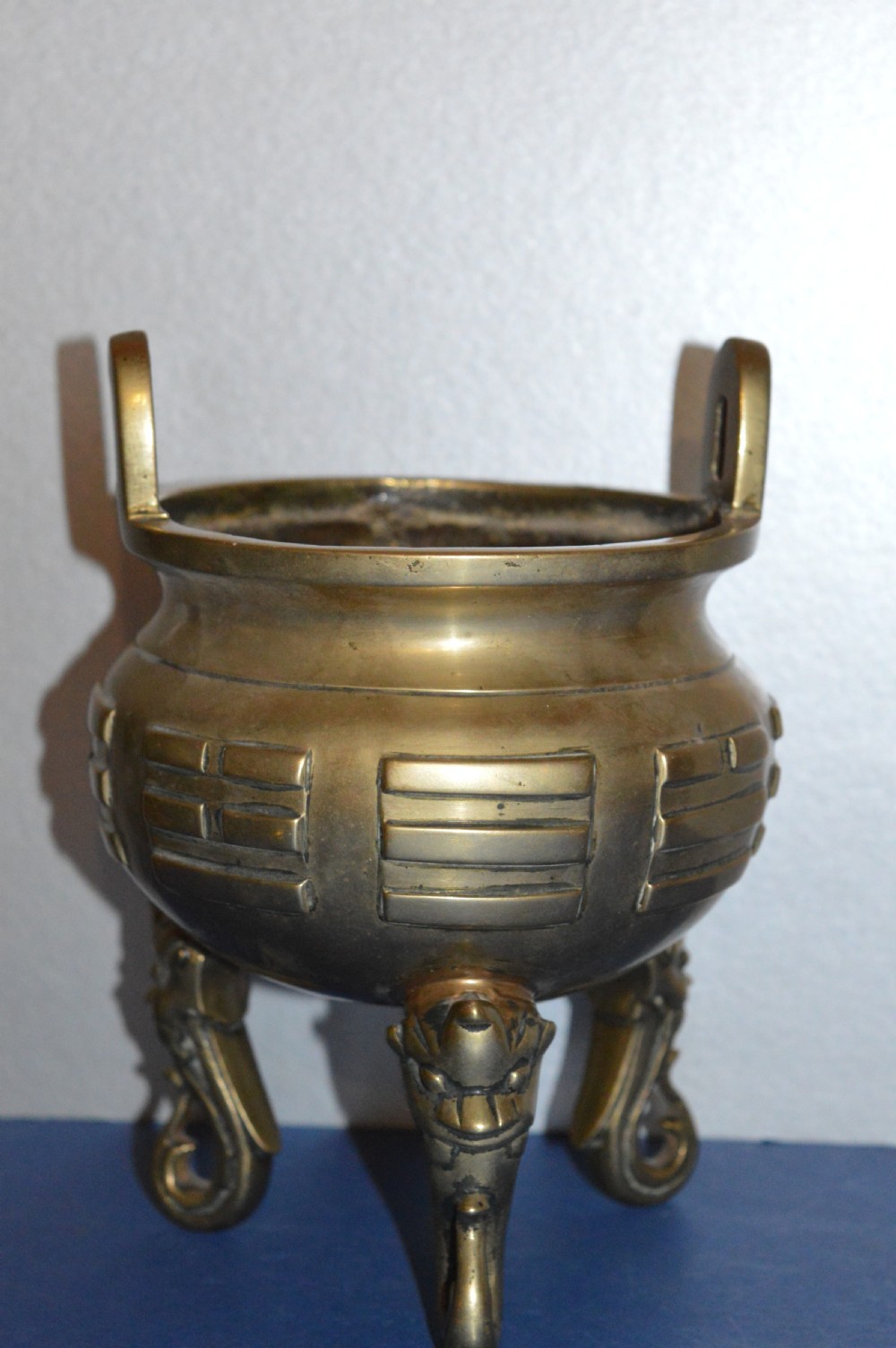 A late nineteenth-century Chinese cast bronze tripod censer featuring raised trigram motifs, upright loop handles, and beast-mask feet.