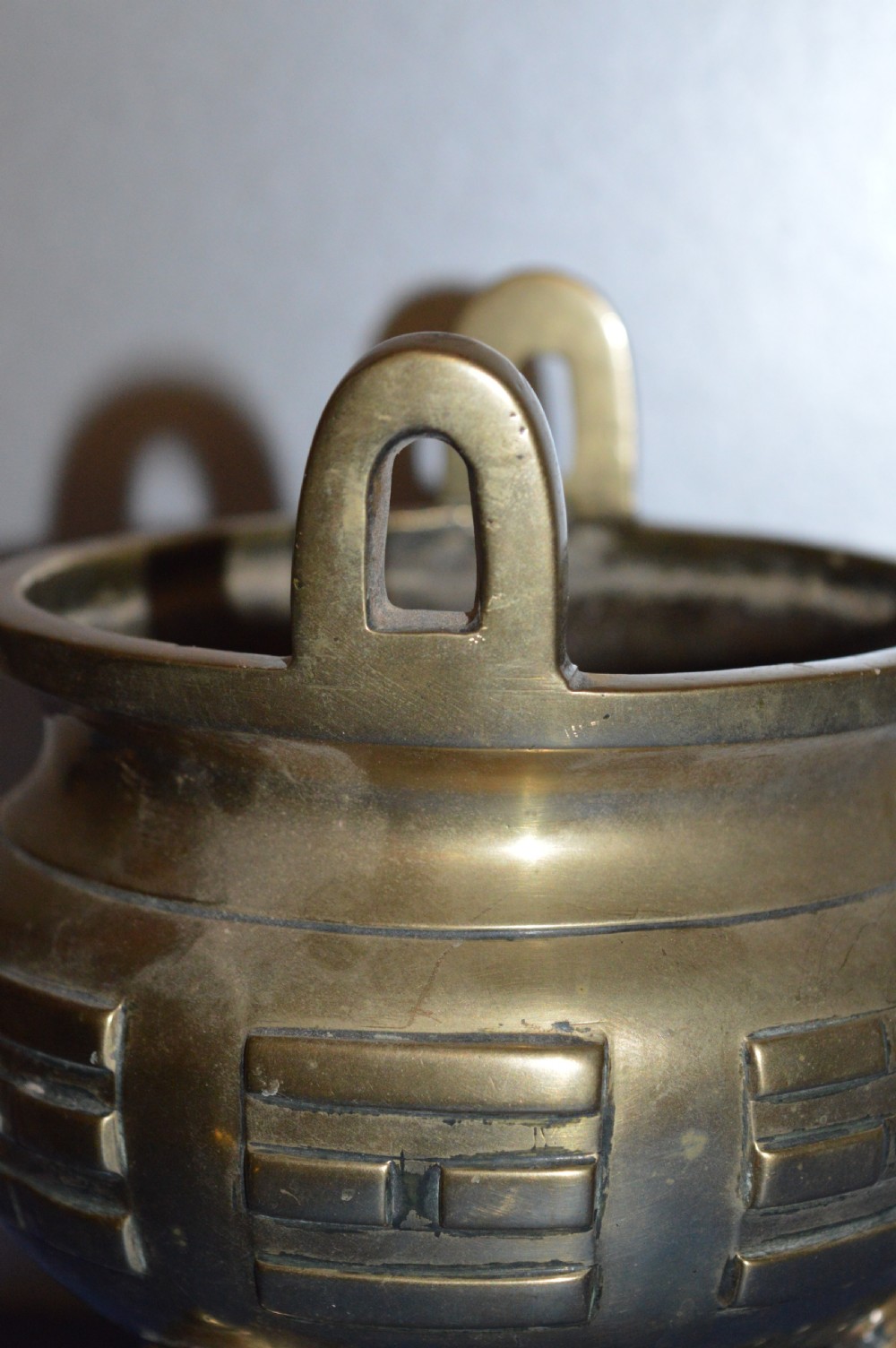 A late nineteenth-century Chinese cast bronze tripod censer featuring raised trigram motifs, upright loop handles, and beast-mask feet. View V