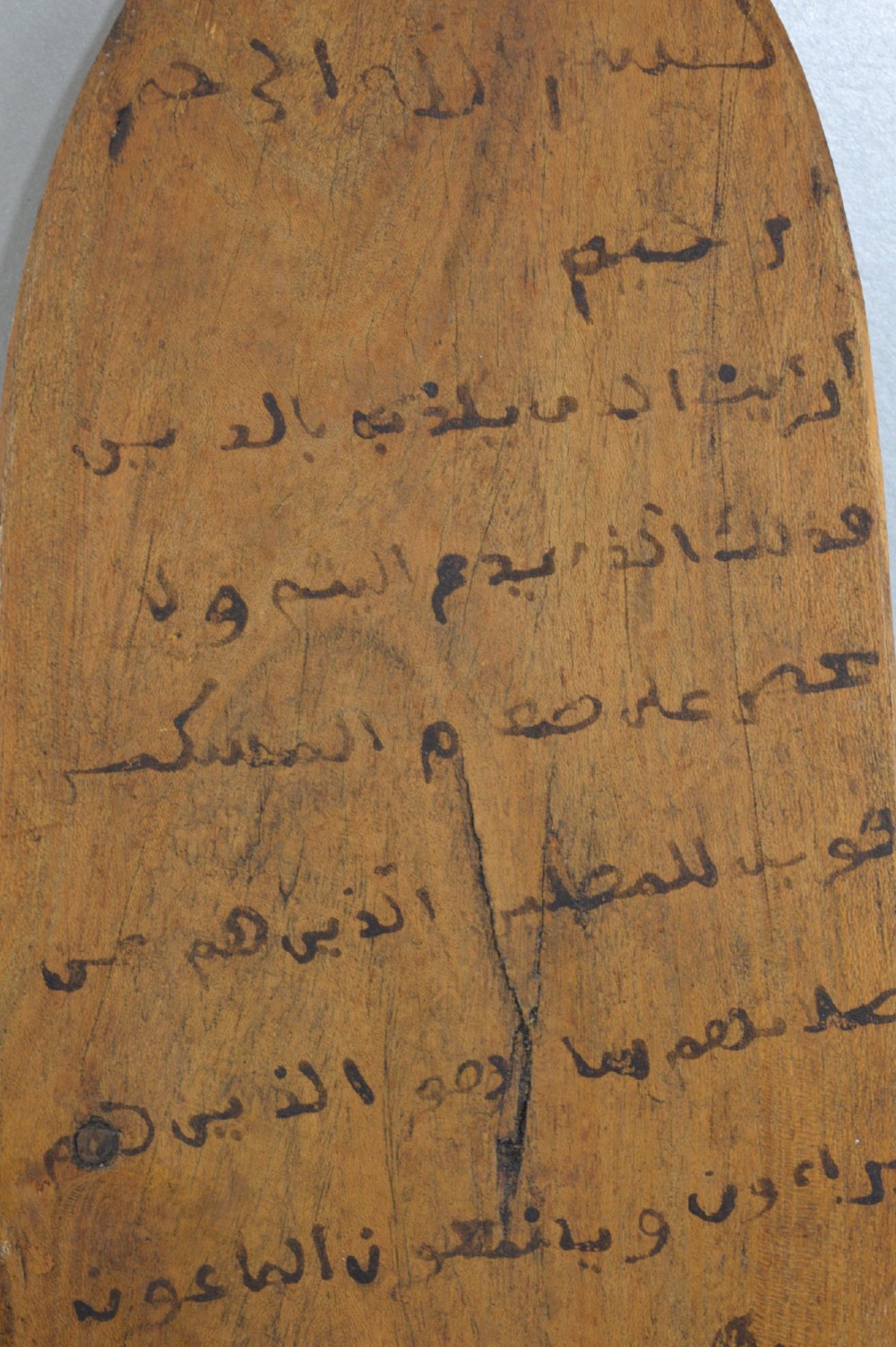 An elongated wooden tablet featuring handwritten Arabic calligraphy in black ink on a natural wood surface. View II