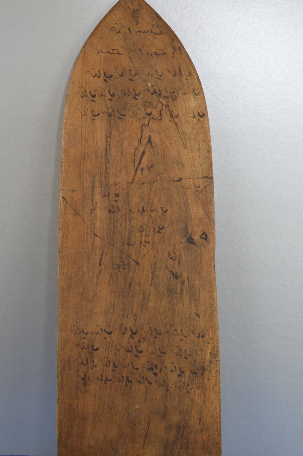 An elongated wooden tablet featuring handwritten Arabic calligraphy in black ink on a natural wood surface. View IV