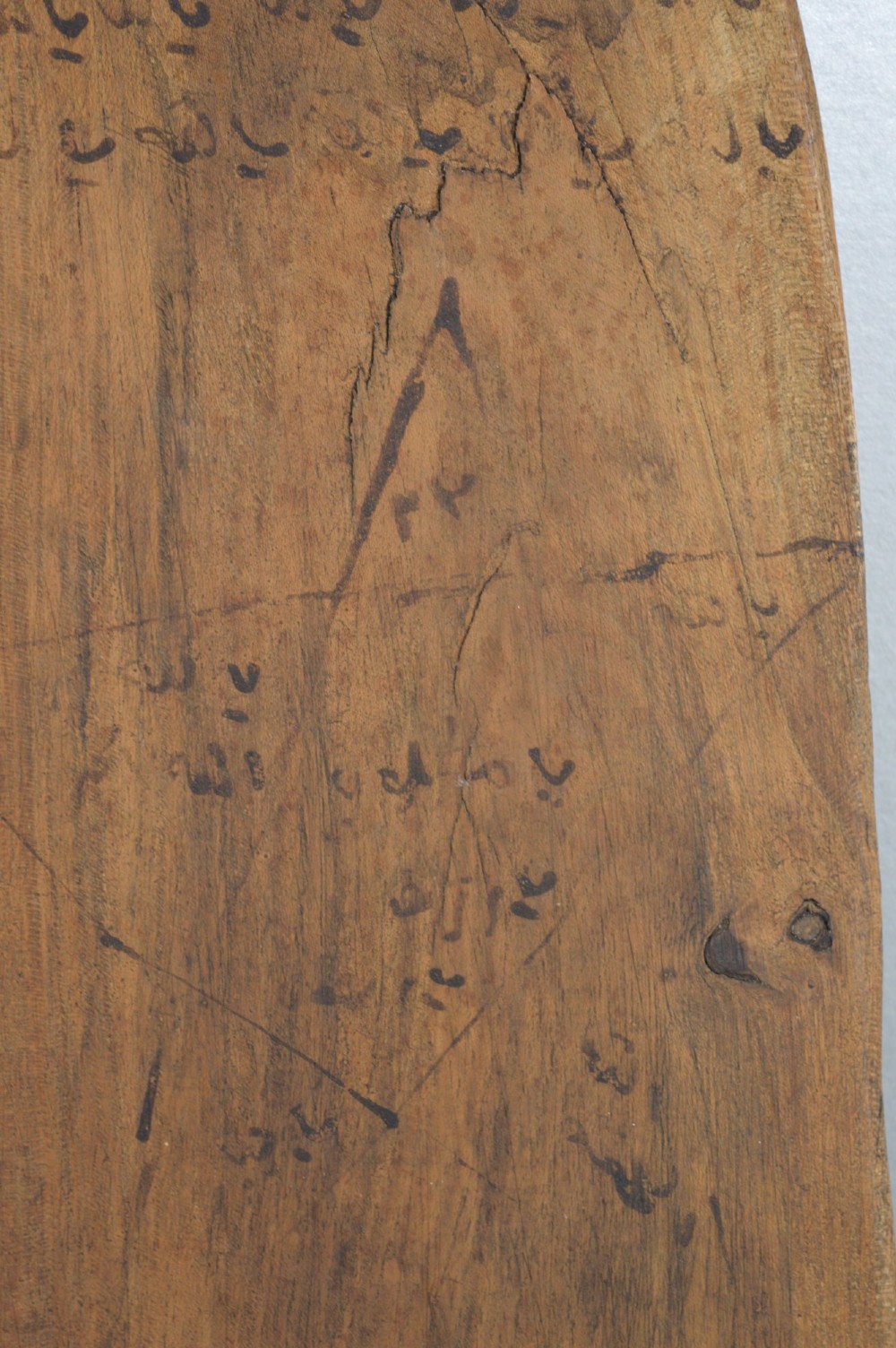An elongated wooden tablet featuring handwritten Arabic calligraphy in black ink on a natural wood surface. View V