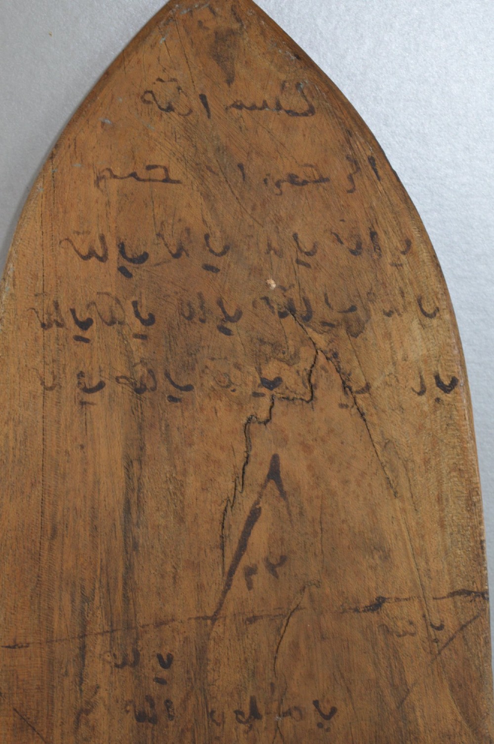 An elongated wooden tablet featuring handwritten Arabic calligraphy in black ink on a natural wood surface. View VI