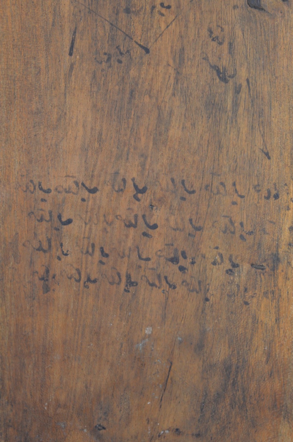 An elongated wooden tablet featuring handwritten Arabic calligraphy in black ink on a natural wood surface. View VII