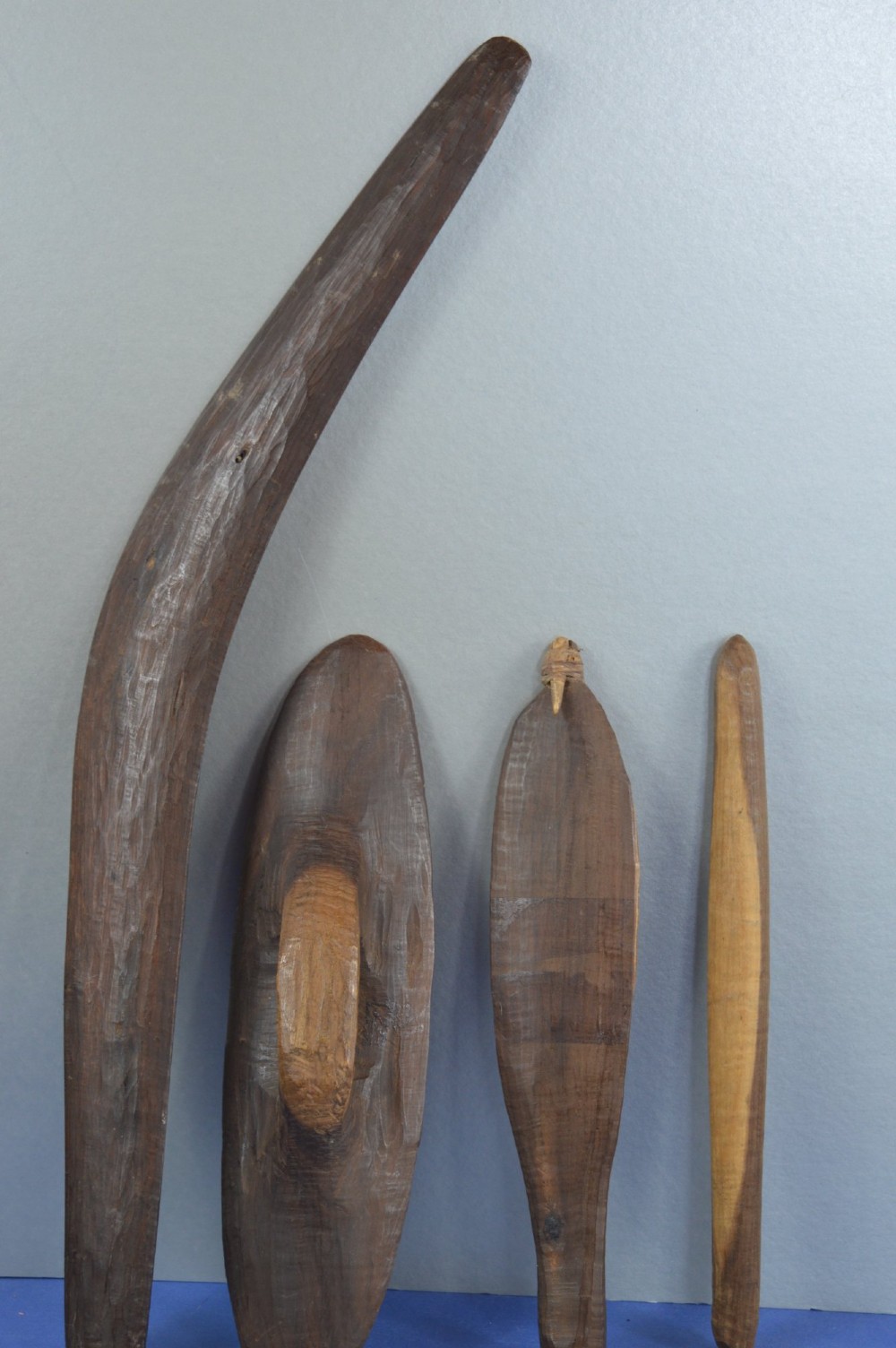 A four-piece set of dark hand-carved wooden Indigenous Australian hunting items, including a boomerang, small shield, spear thrower, and club.