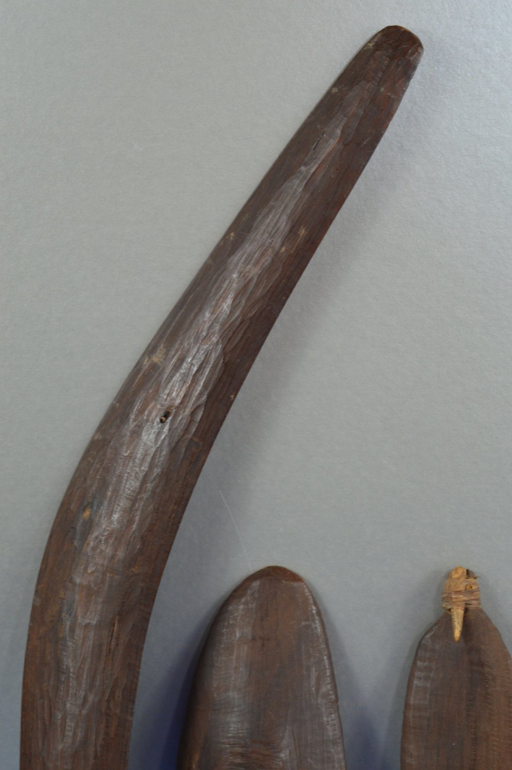 A four-piece set of dark hand-carved wooden Indigenous Australian hunting items, including a boomerang, small shield, spear thrower, and club. View III