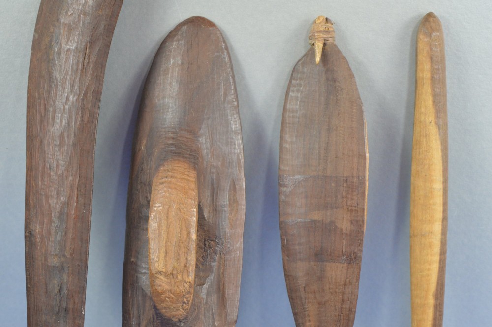 A four-piece set of dark hand-carved wooden Indigenous Australian hunting items, including a boomerang, small shield, spear thrower, and club. View IV