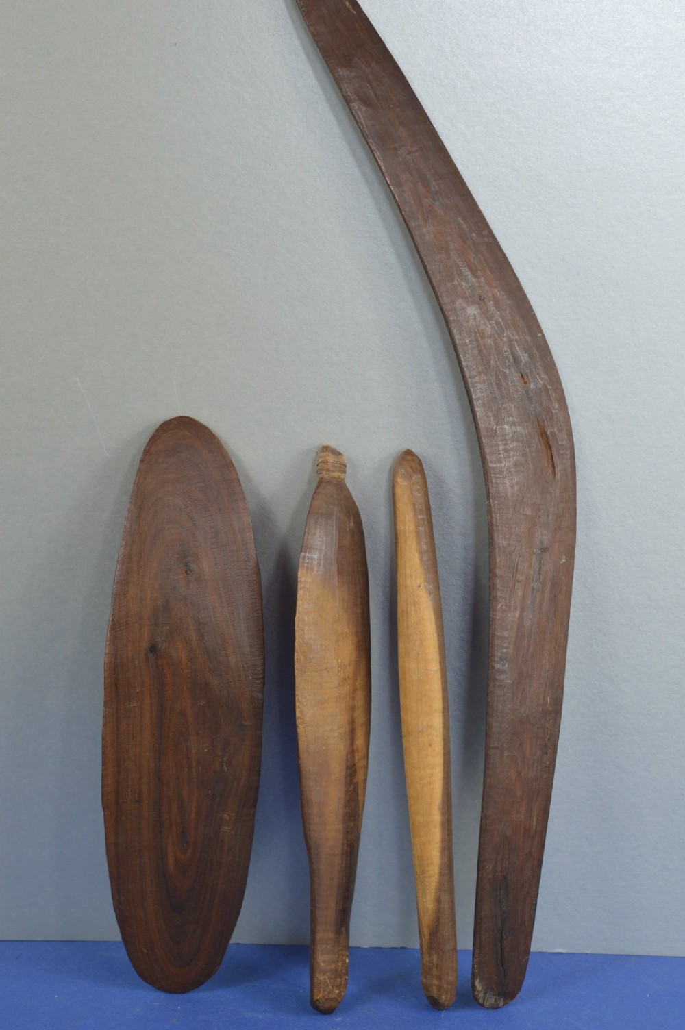 A four-piece set of dark hand-carved wooden Indigenous Australian hunting items, including a boomerang, small shield, spear thrower, and club. View VI