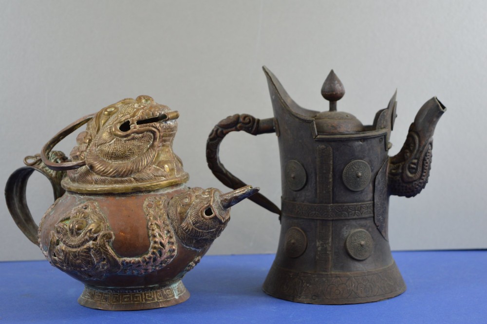 A pair of 19th-century Tibetan metal vessels comprising a squat copper pot with a snow lion lid and a tall cylindrical brass ewer with a dragon spout.