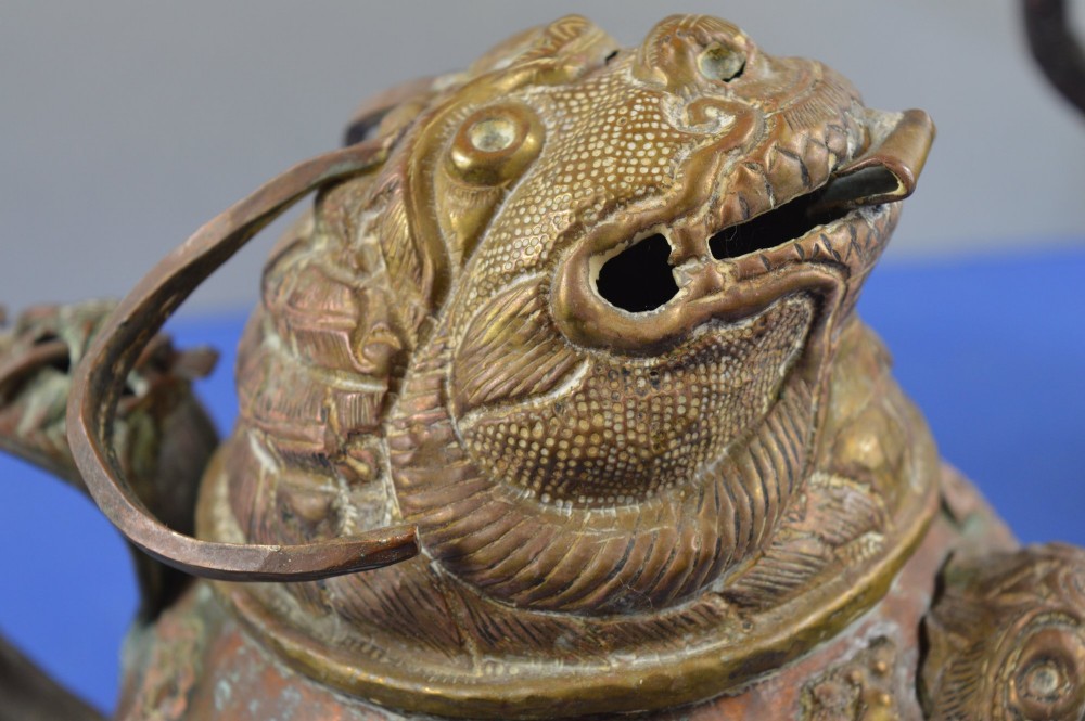 A pair of 19th-century Tibetan metal vessels comprising a squat copper pot with a snow lion lid and a tall cylindrical brass ewer with a dragon spout. View II