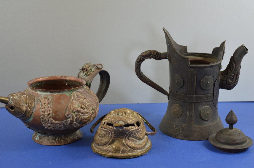 A pair of 19th-century Tibetan metal vessels comprising a squat copper pot with a snow lion lid and a tall cylindrical brass ewer with a dragon spout. View X