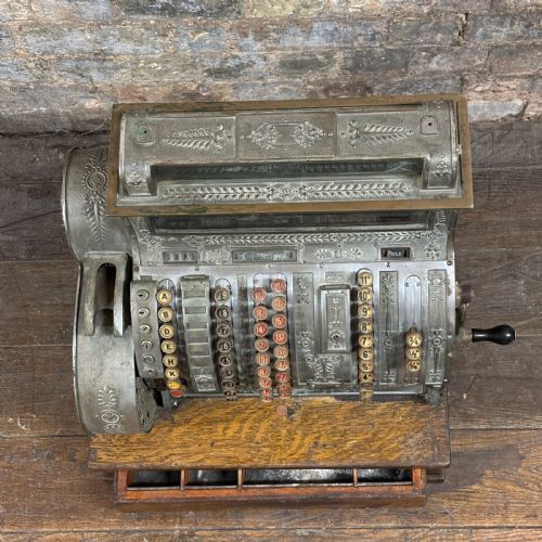 fig 1. An early twentieth-century mechanical cash register featuring a cast metal case on a wooden base with an open currency drawer.