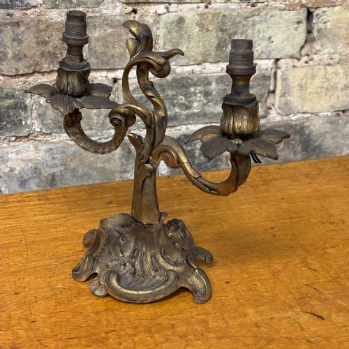 fig 1. A two-arm gilt brass table lamp base featuring sculpted leaf motifs, curved organic branches, and a broad scrolling base.