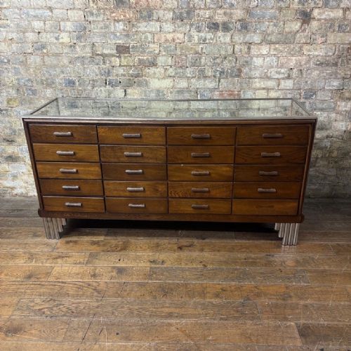 fig 1. A 1930s Art Deco haberdashery counter featuring a clear glass top and sides, a chrome frame with stepped feet, and twenty internal oak display drawers.