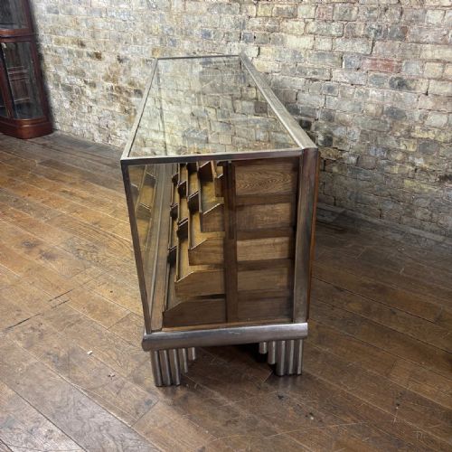 fig 2. A 1930s Art Deco haberdashery counter featuring a clear glass top and sides, a chrome frame with stepped feet, and twenty internal oak display drawers.