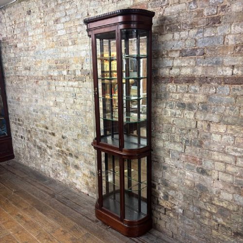 fig 1. A tall Edwardian mahogany two-part display cabinet with curved glass sides, glazed doors, adjustable glass shelves, and brass escutcheons.