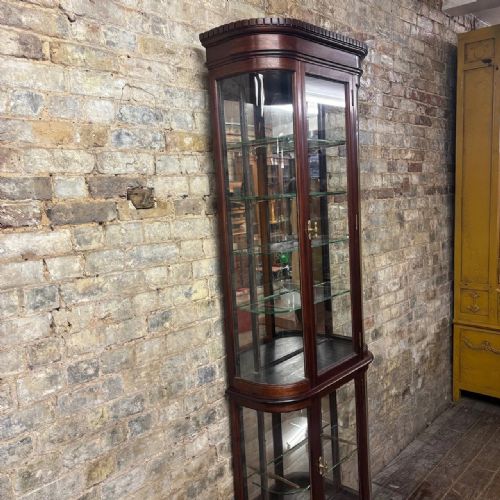 fig 2. A tall Edwardian mahogany two-part display cabinet with curved glass sides, glazed doors, adjustable glass shelves, and brass escutcheons.