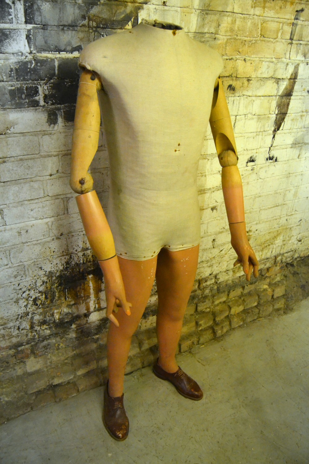 A full-length 1920s male mannequin featuring a canvas torso, articulated wooden arms, painted legs, and leather shoes.